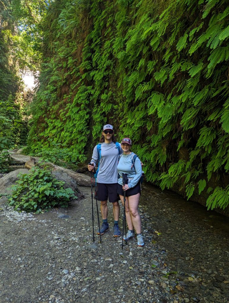 Molly and JD posing in front of a wall of ferns.